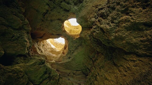 Natural twin skylights illuminate the rugged limestone interior of Devils Eyes Cave on the Algarve coast of Portugal.