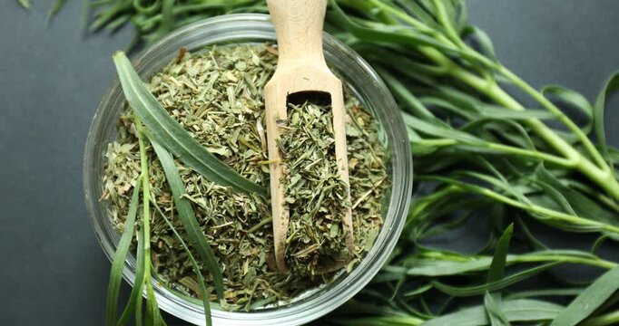 Dried and fresh tarragon in bowl on black surface background, top view