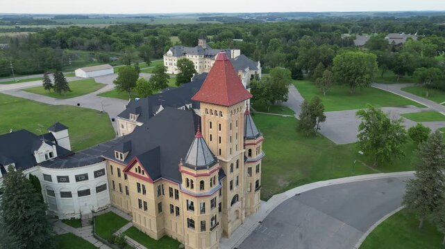 Aerial drone footage circling the main entrance of a long abandoned medical facility. A mental institution built in the 1890s and since retired. Large imposing colored towers surrounded by grounds
