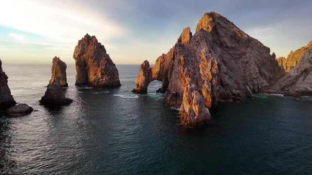 Aerial drone shot of The Arch of Cabo San Lucas at sunrise with fishing boat passing by granite cliffs in Mexico