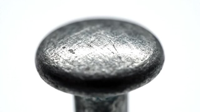 Extreme close-up macro shot of a metallic nail head showing surface texture and detail with white background