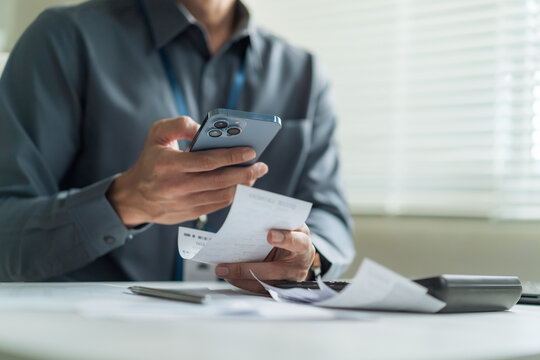 Close-up of office worker using smartphone to scan receipt and expense bill for mobile tracking at desk.