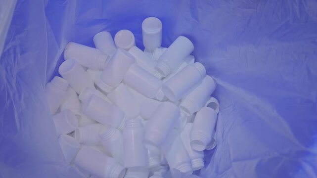 Empty white plastic bottles are falling into a large pile, heap from conveyor belt of bottle injection blow molding machine at factory, plant - close up