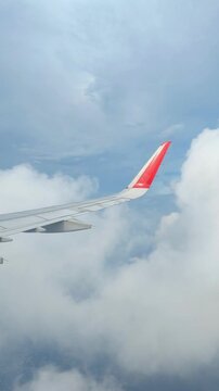 Vertical video of an airplane wing viewed from a passenger window above dramatic clouds and blue sky, capturing a scenic commercial flight and air travel experience.