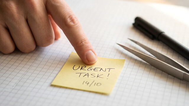 Close up of hand pointing to urgent task reminder note on office desk