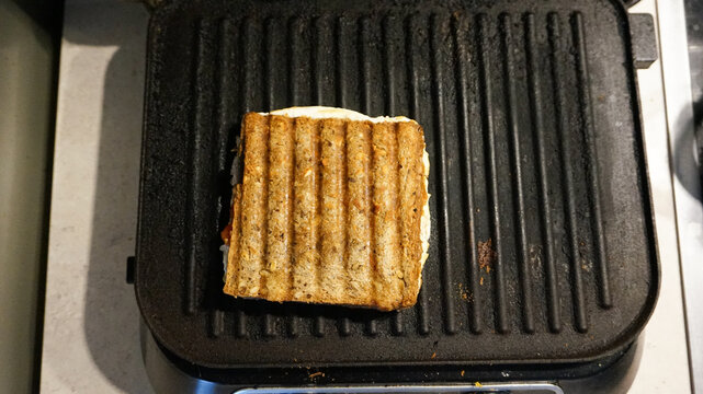 Overhead view of a delicious grilled cheese sandwich with golden grill marks cooking on an electric home grill.