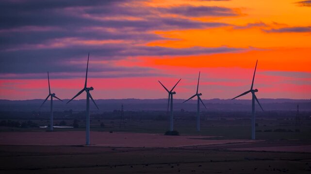 Wind turbines silhouetted against a fiery sunset over rural Sussex, England; ideal for renewable energy, sustainability, climate, technology and business advertising