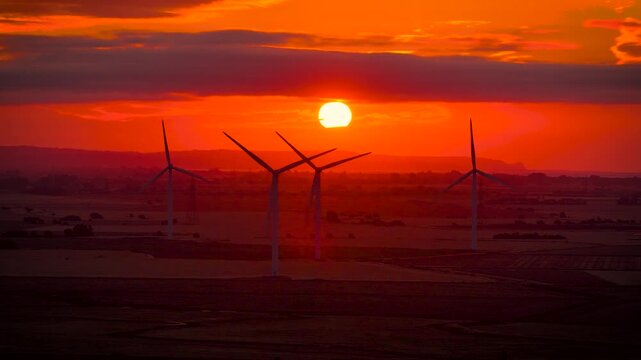 Wind turbines silhouetted against a fiery sunset over rural Sussex, England; ideal for renewable energy, sustainability, climate, technology and business advertising