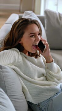 Young woman smiling while talking on smartphone on couch at home, vertical shot