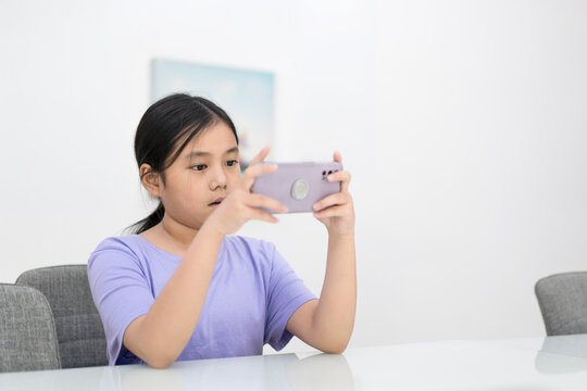 asian child playing game on smartphone or kid girl holding looking mobile phone and addicted to hyperactive ADHD or youth people esports competition by phone and technology on white room background
