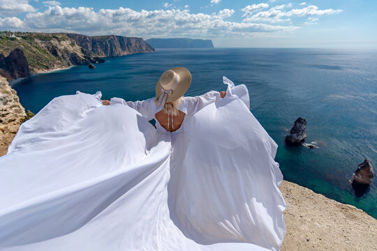 Woman dress hat, woman wearing long white dress and straw hat standing on cliff edge looking at ocean view freedom