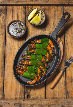 Shrimps cooked in a cast iron pan on a wooden table, garnished with lemon slices and sauce
