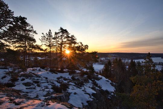 Golden sunrise bursting over a snowy winter forest in Dalsland, Sweden, with vibrant sun rays illuminating a frozen landscape and pine trees under a warm orange and yellow sky