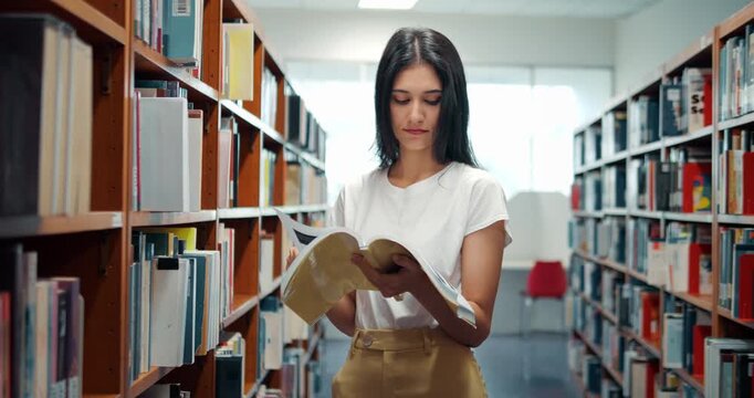 Young woman reads quietly between library shelves. She focuses intently on open pages, absorbed in content. Soft light illuminates her calm