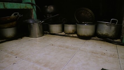 Fototapeta premium Dirty kitchen with messy metal pot utensils, unhygienic lifestyle. A collection of various metal cooking pots arranged on a tiled kitchen floor.