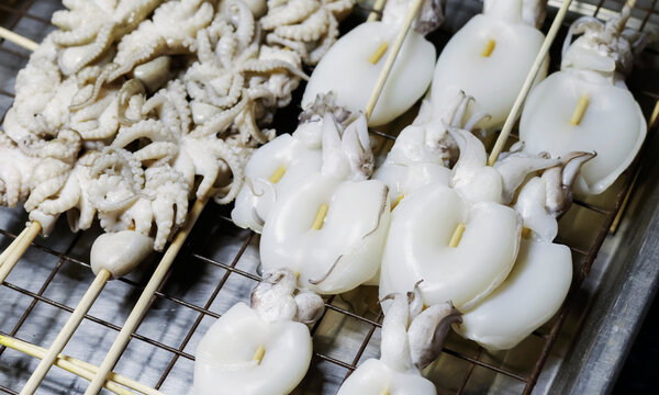 Fresh squid skewers displayed at a seafood market stall, ready for grilling or cooking. Traditional street food ingredients, raw seafood