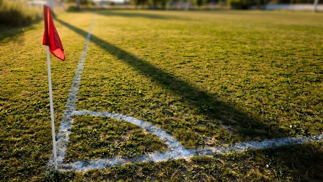 Red corner flag on a grass sports field at golden hour with white boundary line markings
