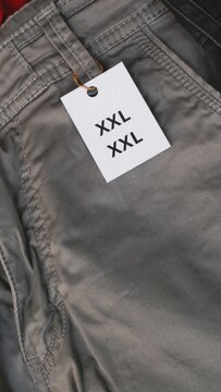 Close up of grey trousers with a white XXL size tag attached.