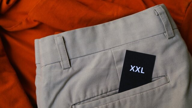Close up of a black XXL size tag tucked into a pair of beige trousers.