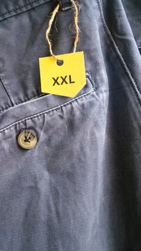 A yellow size XXL clothing tag attached to a pair of blue cotton trousers.