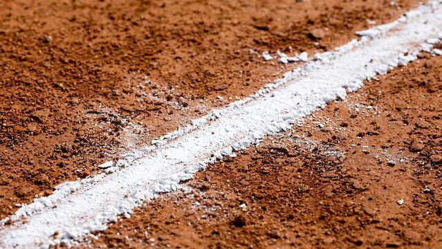 Close-up of a white chalk boundary line on a red clay tennis court surface