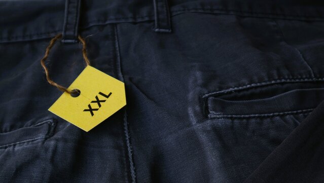 A yellow XXL size tag attached to a pair of dark blue denim jeans.