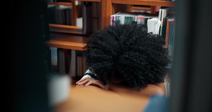 Young girl sits quietly in library stacks. She rests head on folded arms, eyes closed. Curled posture suggests deep thought or fatigue