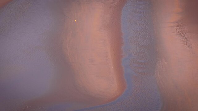Aerial view of low tide sands with flowing tidal channels and soft beach textures in warm light; ideal for travel, nature, background and coastal advertising