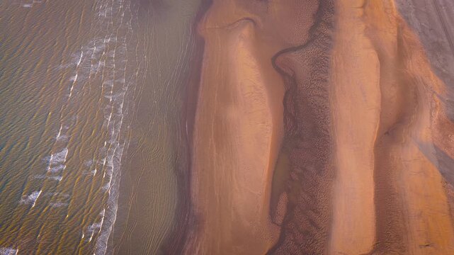 Aerial view of low tide sands with flowing tidal channels and soft beach textures in warm light; ideal for travel, nature, background and coastal advertising