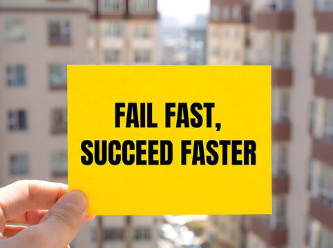 Fail Fast Succeed Faster Motivational Quote On Bright Yellow Card Held By Hand With Blurred Cityscape Background Representing Business Growth, Innovation, And Entrepreneurial Success