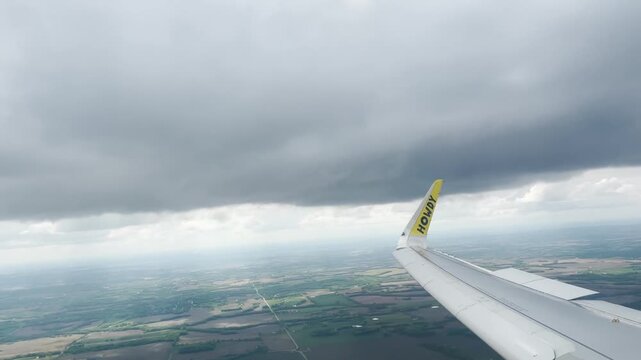 Airplane wing extending over the landscape demonstrates travel efficiency as the steel structure cuts through the thick overcast layer during a commercial flight across the expansive regional terrain.