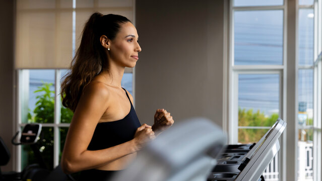 Focused young woman running on a treadmill in a modern condo gym, showcasing an active and healthy lifestyle. Side view of fit woman using treadmill in bright residential fitness room.