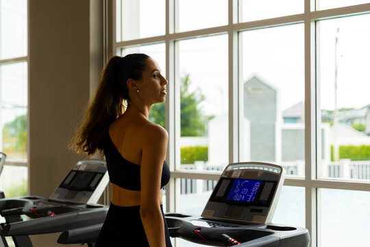 Focused young woman running on a treadmill in a modern condo gym, showcasing an active and healthy lifestyle. Side view of fit woman using treadmill in bright residential fitness room.
