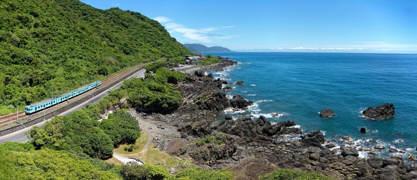 Scenery of "Sea Breeze" express train traveling on railway between the beautiful rocky beach and green wooded mountains in Beiguan Tidal Park on a sunny summer day, in Toucheng, Yilan, Taiwan, Asia