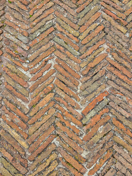 Top-down view of an ancient weathered red brick floor laid in a classic herringbone pattern, creating a rustic background texture.