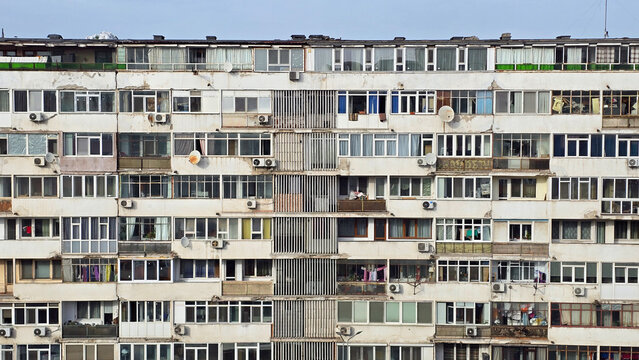 Weathered, multi-story apartment building facade in Bucharest. Rows of windows, AC units, and balconies. Architectural detail, urban texture.