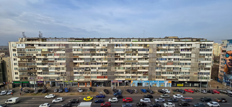 Bucharest, Romania - March 11, 2025: Large, aged apartment building in Bucharest, Romania. Rows of windows, AC units, ground-level shops.