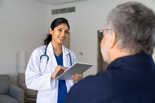 South Asian doctor holding digital tablet, asks questions, records information, listening to patient explaining health condition, symptoms during clinic consultation. professional medical assessment