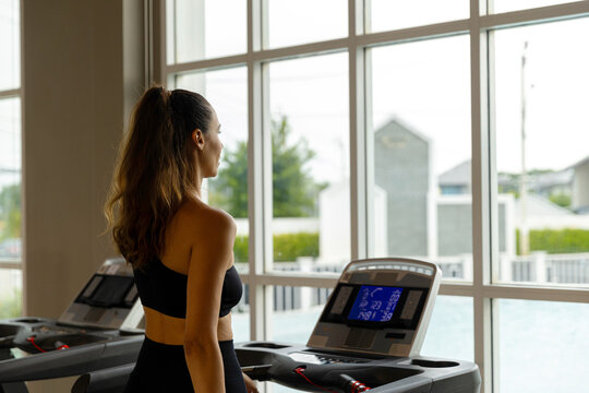 Focused young woman running on a treadmill in a modern condo gym, showcasing an active and healthy lifestyle. Side view of fit woman using treadmill in bright residential fitness room.