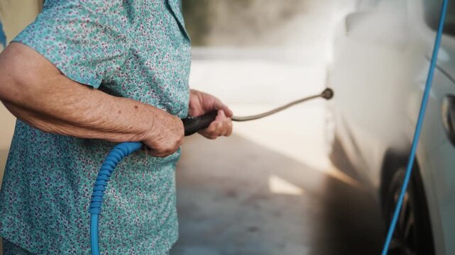 Adult daughter presses the start button as her active senior mother begins washing their car at a self-service car wash.