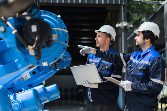 Robotic system integrator team reviews blue robotic arm at warehouse. inspection, quality assurance before delivery.