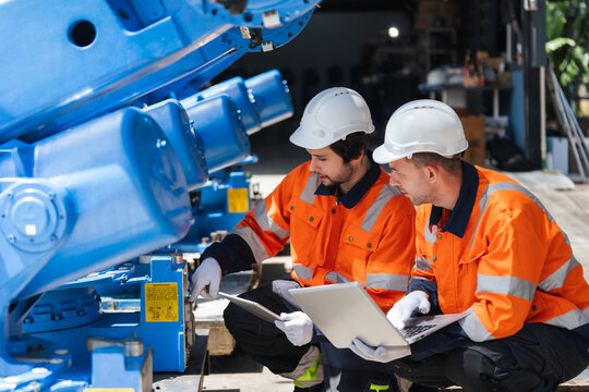 Two robotics technician inspect blue robotic arm with laptop and tablet before delivery. performing machinery diagnostics, supporting robotic system integration, plant engineering