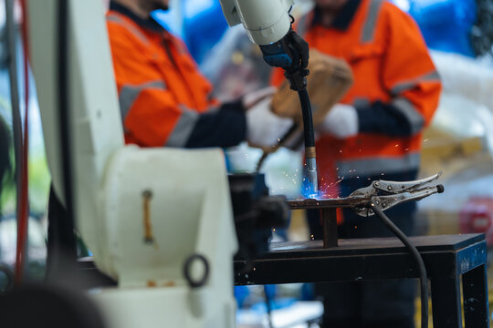 Close-up Robot torch of automation robotic arm welding sparks on clamped steel fixture, Robotic welding arm test performs precision welding before delivery.