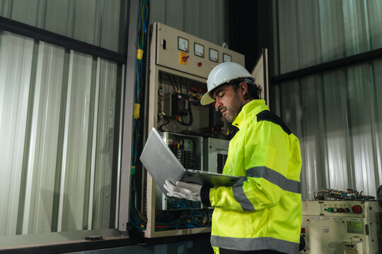 Preventive maintenance Electrical technician using laptop working electrical system inspection beside control panel in factory. diagnostics, troubleshooting, safety, preventive service.
