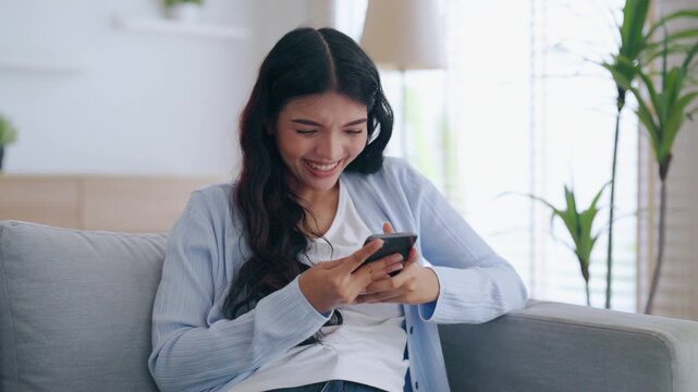 Happy young asian woman relax on comfortable couch at home texting messaging on smartphone, smiling girl use cellphone, chatting online message, shopping online from home