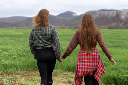 Hiking couple walking hand in hand through green field toward distant mountains under cloudy sky