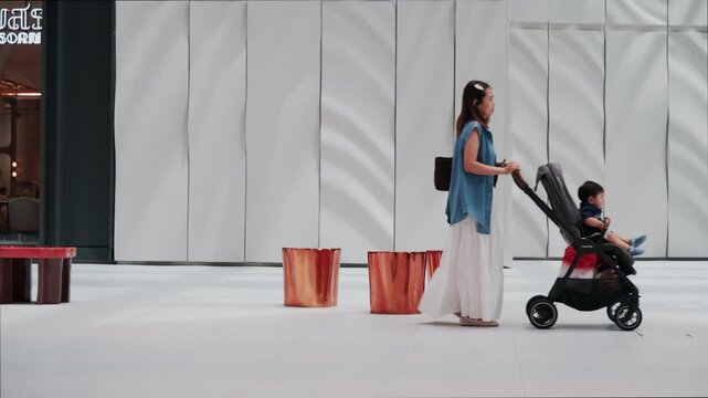 Asian family mother and child with baby carriage in modern shopping mall hall.	
