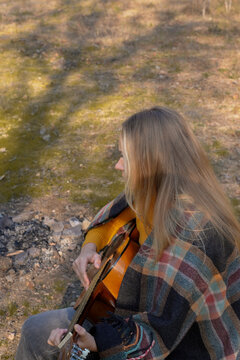 Blonde woman playing string guitar outdoors in autumn forest. Concept of sound therapy, mental health and wellness rituals. Calmness tranquility audio-sensory practices. Aura farming energy holistic