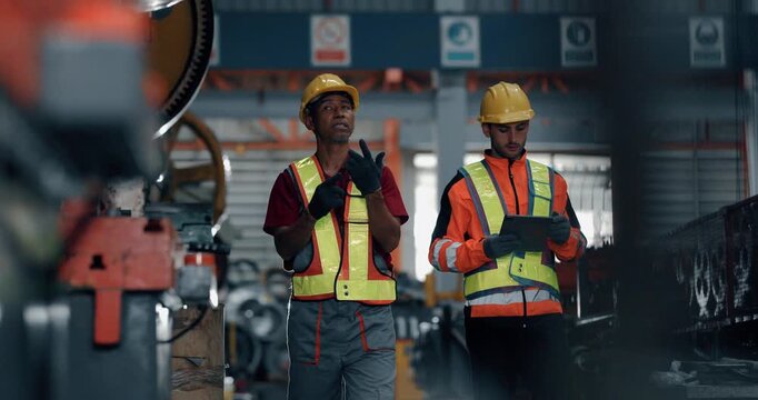 Two engineers inspecting large industrial gear of press machine with tablet in factory