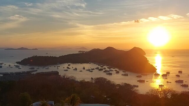 High angle view of a breathtaking golden sunset over the tropical sea of Labuan Bajo, East Nusa Tenggara, Indonesia. The warm sun casts a bright reflection on the water surface, illuminating numerous 
